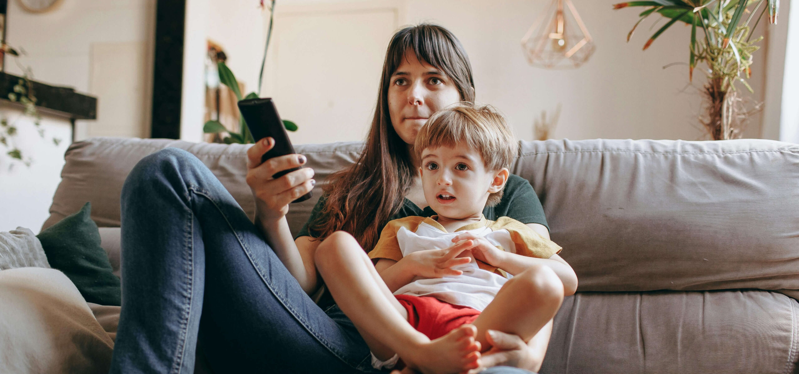 child and mother watching tv together while sitting on couch scaled